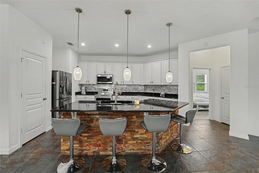 A kitchen features white cabinets, black granite countertops, a stone-faced island, and four bar stools — 2912 BOATING BOULEVARD, KISSIMMEE, FL