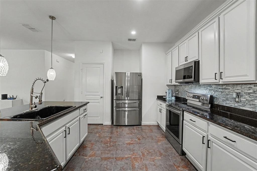 A kitchen features white cabinets, dark granite countertops, stainless steel appliances, and tiled flooring — 2912 BOATING BOULEVARD, KISSIMMEE, FL