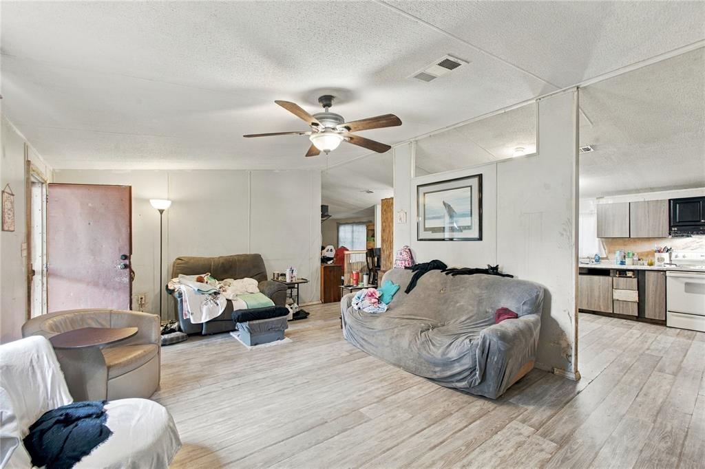 A living room with light wood-look flooring, a ceiling fan, and an adjacent kitchen area — 3608 VALLEY TRAIL, LAKELAND, FL