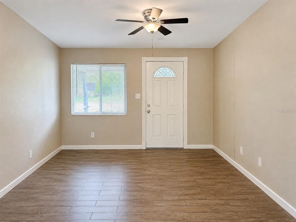 A room with light-colored walls, wood-look tile flooring, a ceiling fan, and a front door — 8836 79TH PLACE, SEMINOLE, FL