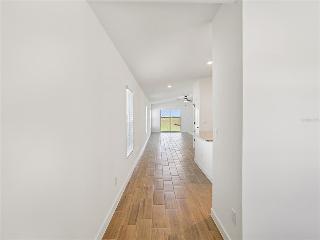 A long hallway with wood-look tile flooring leads toward a window with a backyard view — 5241 CAP ROAD, BROOKSVILLE, FL