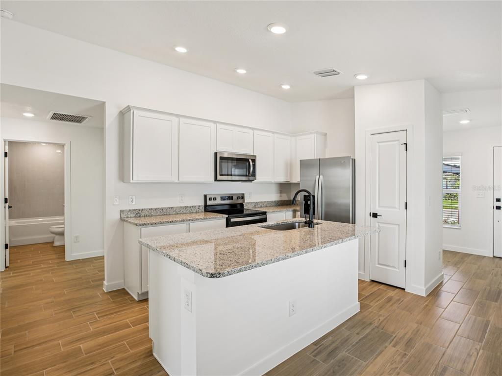 A kitchen features white cabinets, granite countertops, stainless steel appliances, and wood-look tile flooring — 5241 CAP ROAD, BROOKSVILLE, FL