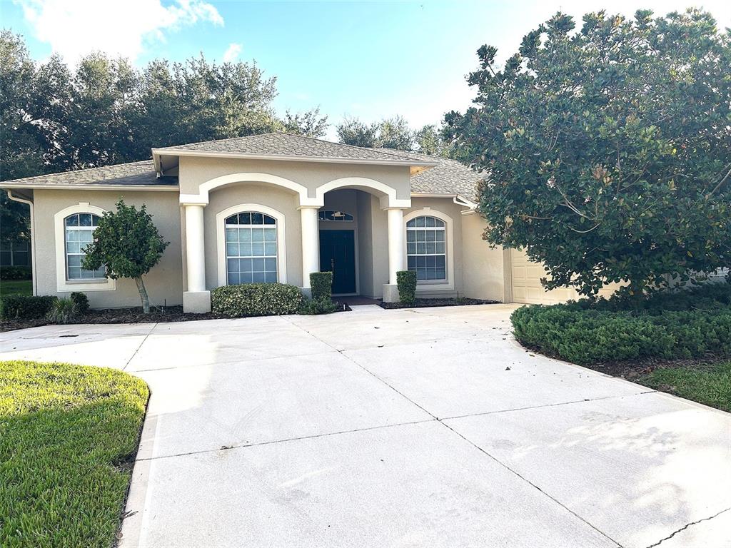 A single-story house with a beige stucco exterior, arched windows, and a concrete driveway — 18754 GRAND CLUB DRIVE, HUDSON, FL