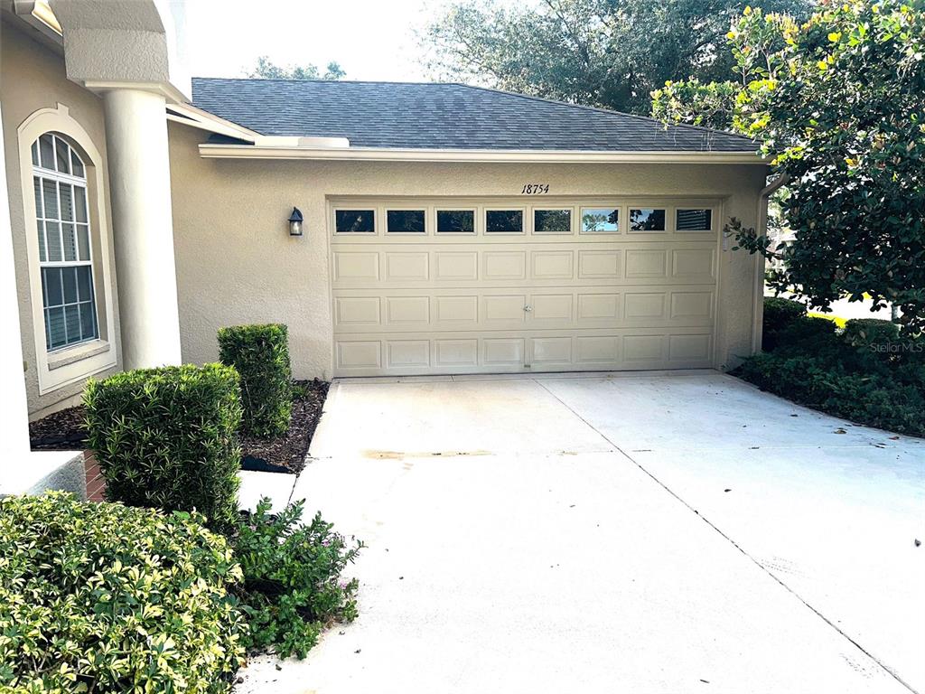 A beige house exterior features a two-car garage with windows and a concrete driveway — 18754 GRAND CLUB DRIVE, HUDSON, FL