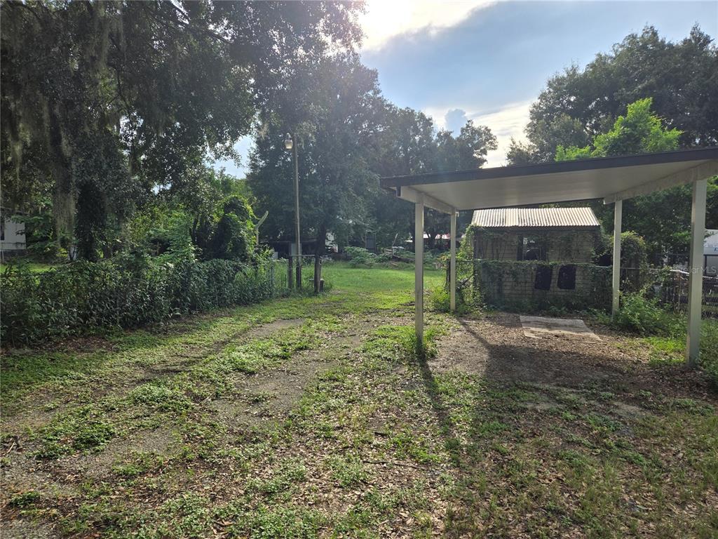 A gravel driveway leads to a small shed under a metal carport in a yard — 10612 SKEWLEE GARDENS DRIVE, THONOTOSASSA, FL