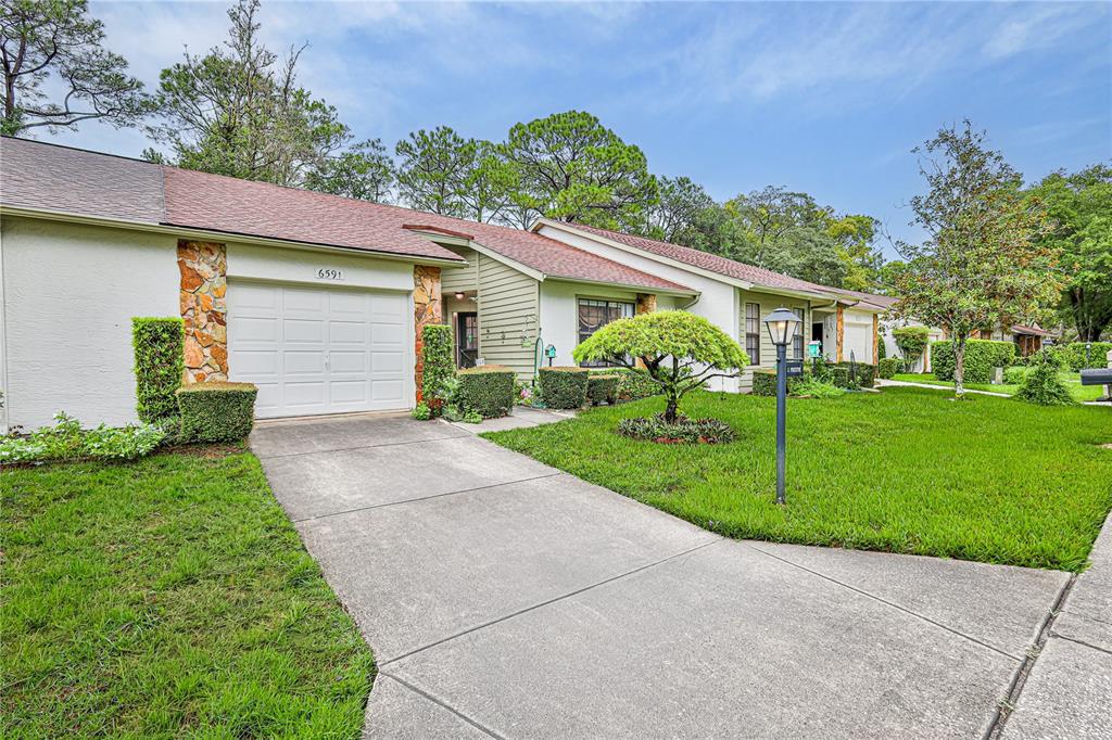 A single-story house with a white garage door, stone accents, and a concrete driveway — 6591 BRAMBLELEAF DRIVE, SPRING HILL, FL