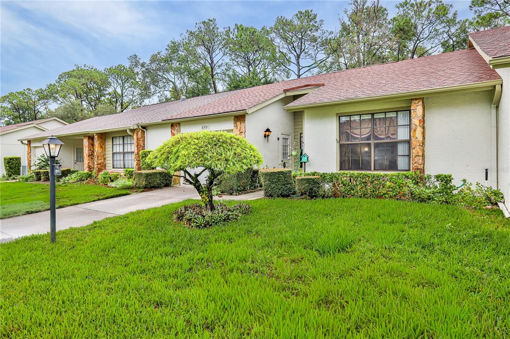 A single-story house with a tan stucco exterior, stone accents, and a green lawn — 6591 BRAMBLELEAF DRIVE, SPRING HILL, FL