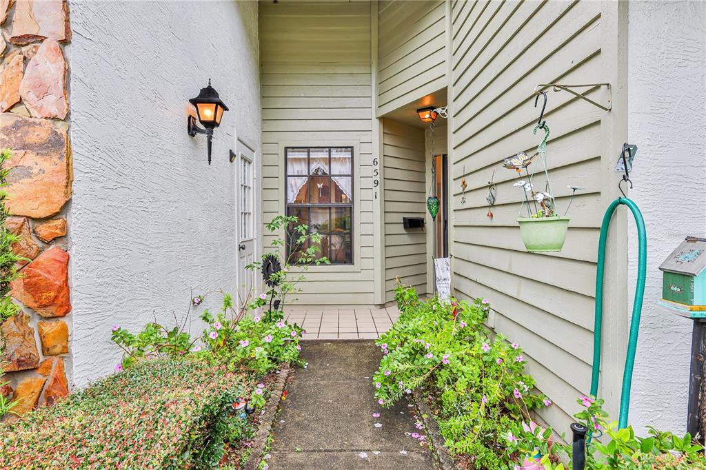 A concrete walkway leads to the front entrance of a house with stone and siding — 6591 BRAMBLELEAF DRIVE, SPRING HILL, FL