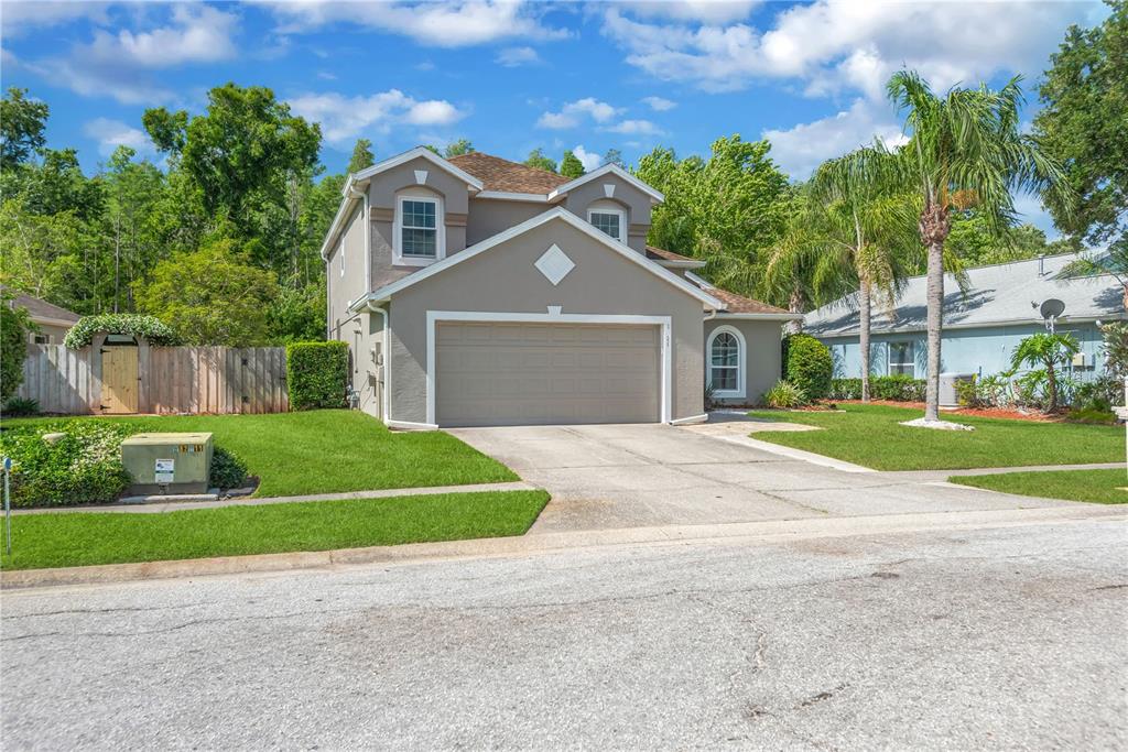 A two-story suburban house with a tan exterior, a two-car garage, and a front lawn — 1211 TIMBER TRACE DRIVE, WESLEY CHAPEL, FL