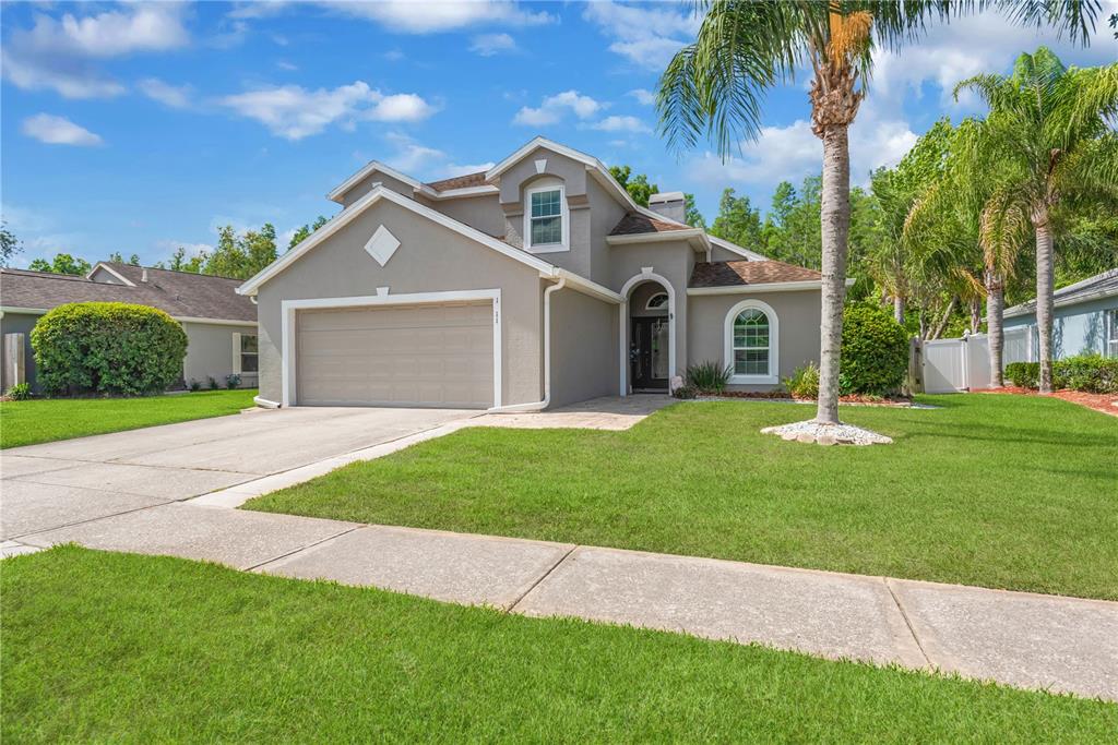 A single-story suburban house with a gray stucco exterior, a two-car garage, and a palm tree — 1211 TIMBER TRACE DRIVE, WESLEY CHAPEL, FL