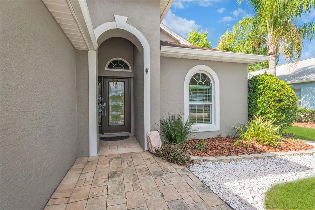 A paved walkway leads to the arched entryway and front door of a gray house — 1211 TIMBER TRACE DRIVE, WESLEY CHAPEL, FL