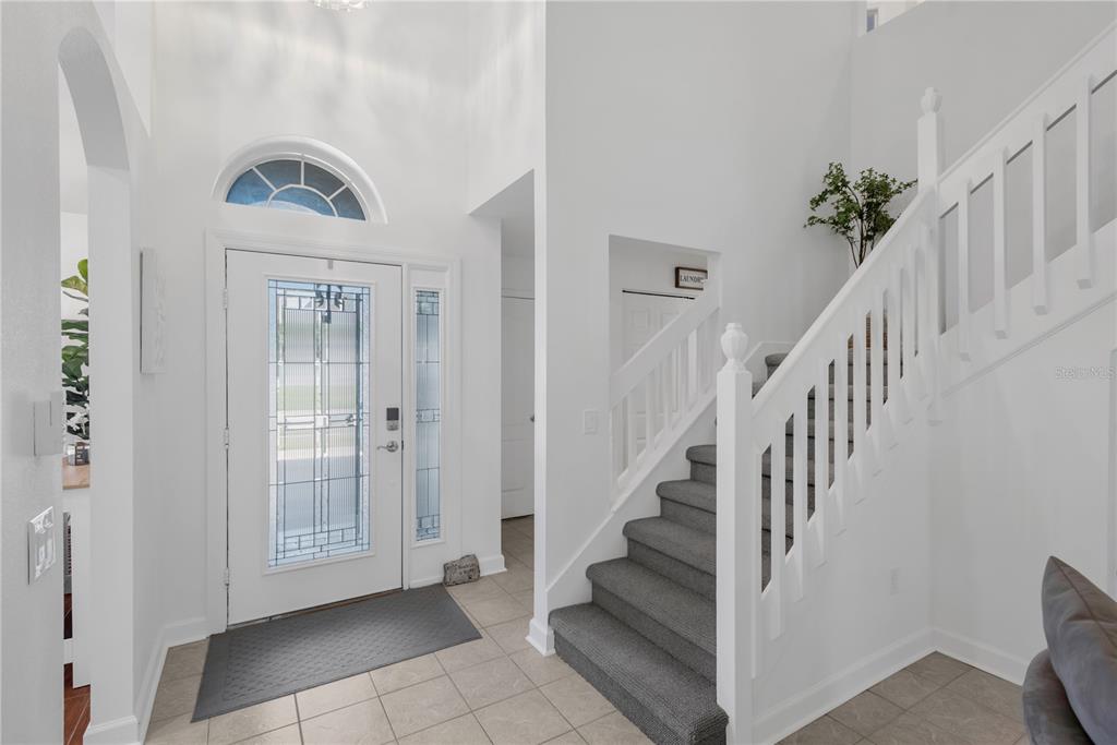 A bright foyer features a white front door, tiled floor, and a carpeted staircase — 1211 TIMBER TRACE DRIVE, WESLEY CHAPEL, FL