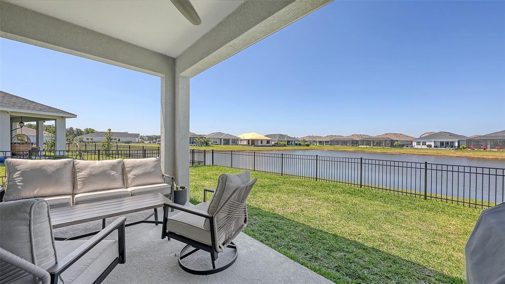A covered patio features outdoor furniture overlooking a fenced backyard and a community pond — 11869 RICHMOND TRAIL, PARRISH, FL