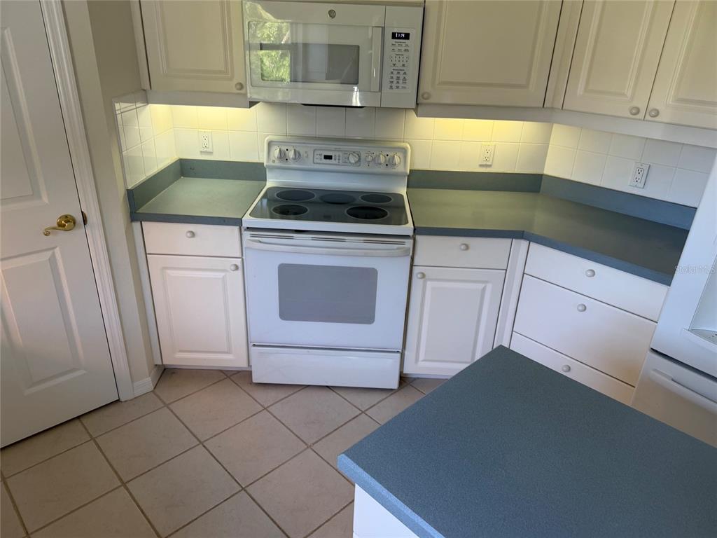 A kitchen with white cabinets, blue countertops, a white stove, and a microwave — 9250 NW 13TH AVENUE CIRCLE, BRADENTON, FL