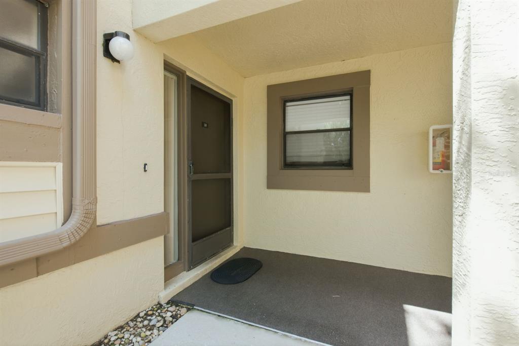 A covered entryway features a dark screen door, a small window, and a wall-mounted fire extinguisher — 10 WOODLAKE PLACE, OLDSMAR, FL