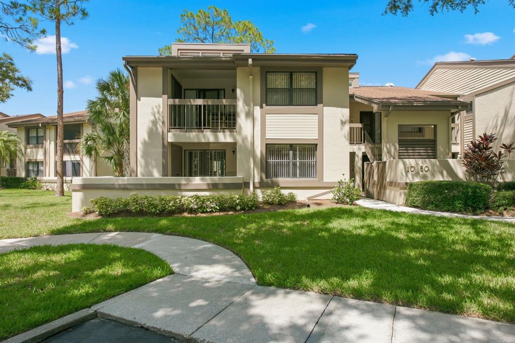 A two-story apartment building exterior with a concrete walkway, green lawn, and balcony — 10 WOODLAKE PLACE, OLDSMAR, FL