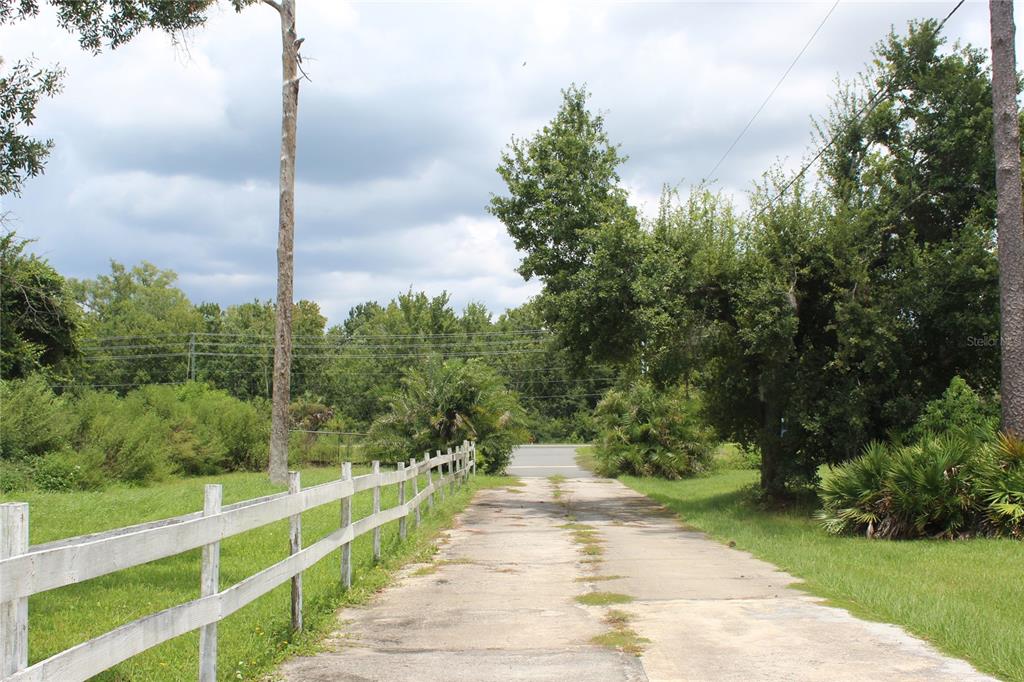 A concrete driveway leads toward a road, bordered by a white fence and lush greenery — 4900 S ORANGE BLOSSOM TRAIL, KISSIMMEE, FL