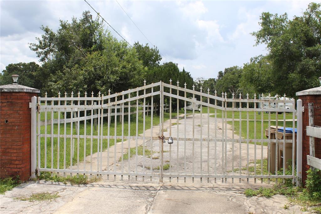 A white metal gate stands between two brick pillars at the entrance of a driveway — 4900 S ORANGE BLOSSOM TRAIL, KISSIMMEE, FL