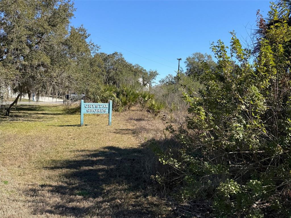 A blue sign reading Crystal Shores stands in a grassy, wooded lot under a clear sky — 10748 W PINE BARK LANE, CRYSTAL RIVER, FL