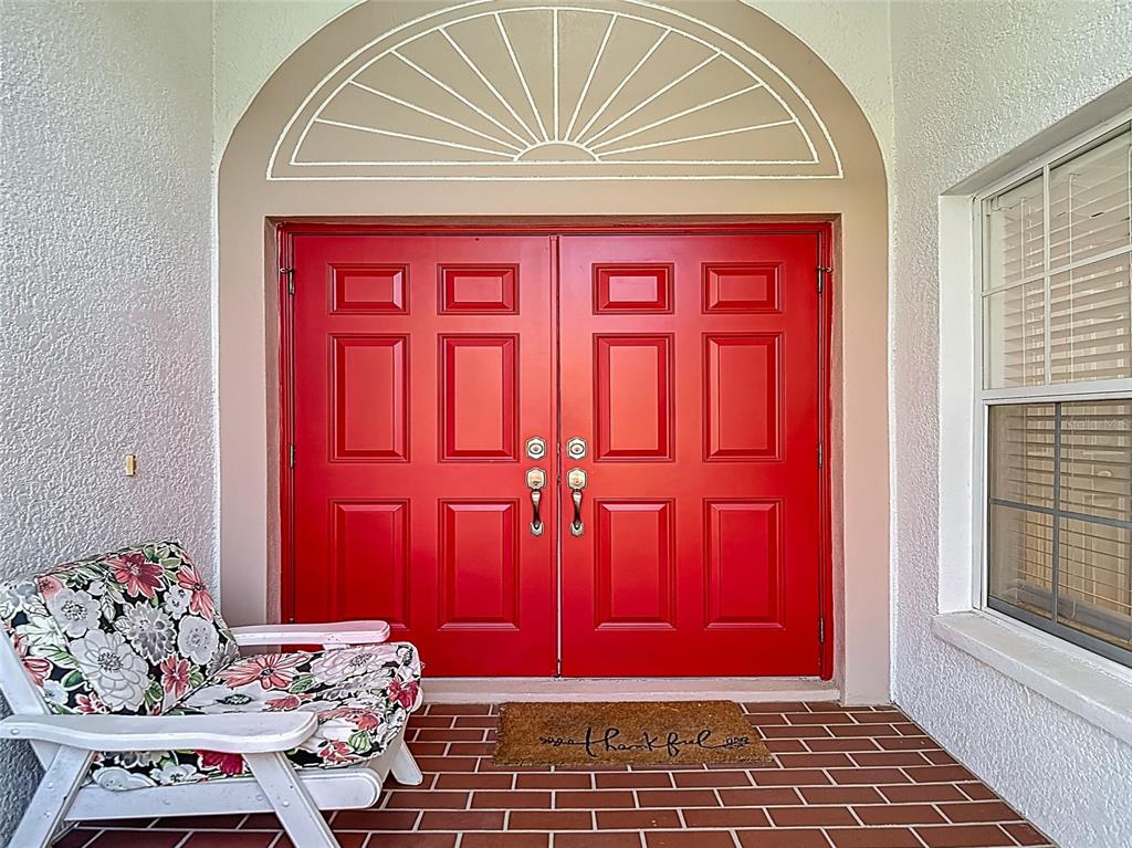 A bright red double front door with a semi-circular transom window on a brick porch — 9608 ROLLING CIRCLE, SAN ANTONIO, FL