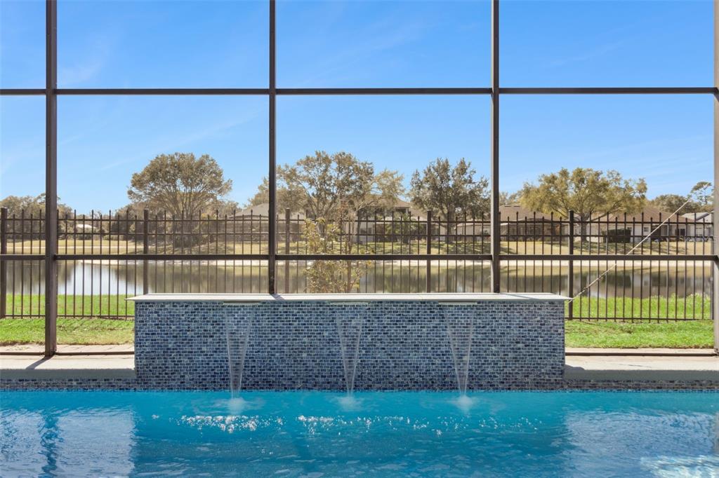 A swimming pool with three water features sits inside a screened enclosure overlooking a lake — 6473 EVERINGHAM LANE, SANFORD, FL