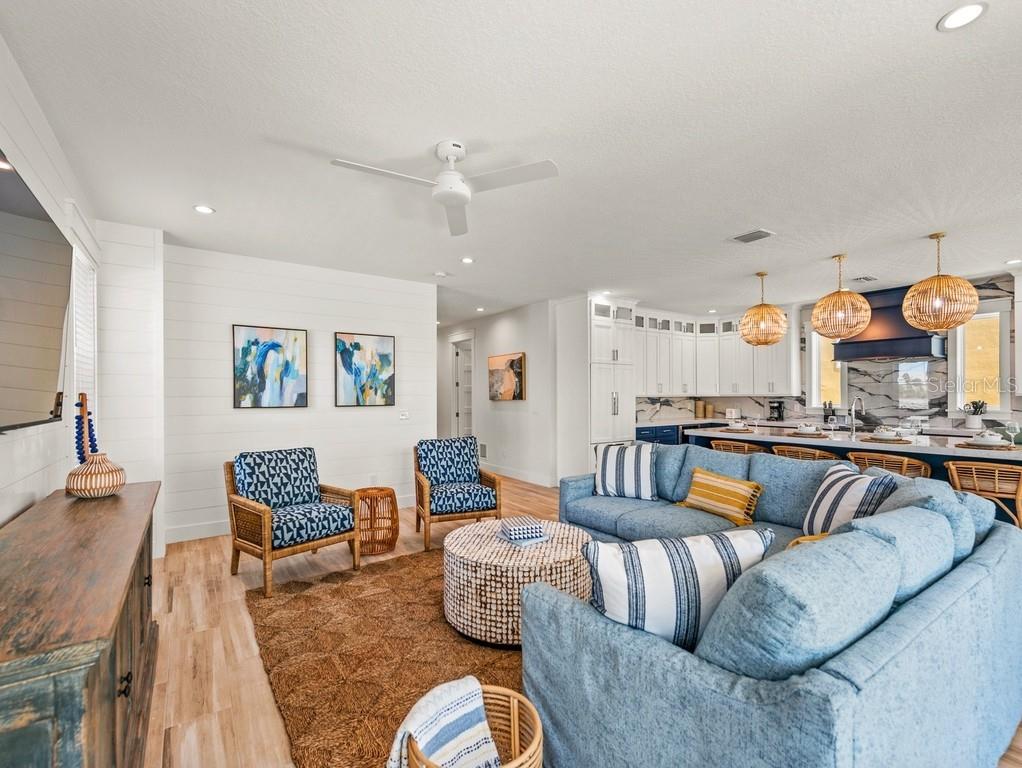 A bright, open-concept living room and kitchen featuring blue furniture, wood floors, and pendant lights — 204 COOLIDGE DRIVE, SARASOTA, FL