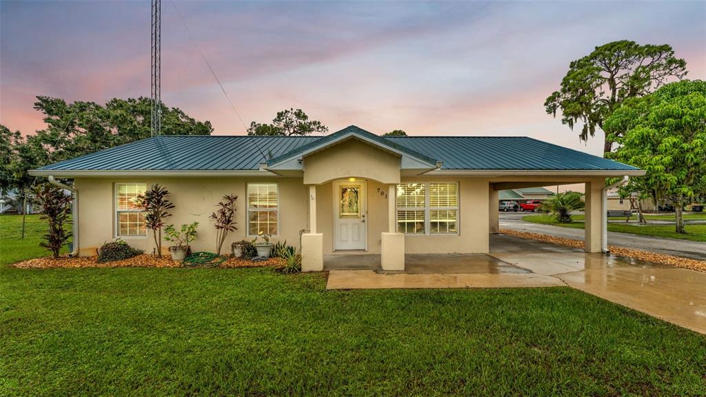 A single-story house with a metal roof, front porch, and attached carport under a sunset — 701 KEEN ROAD, FROSTPROOF, FL