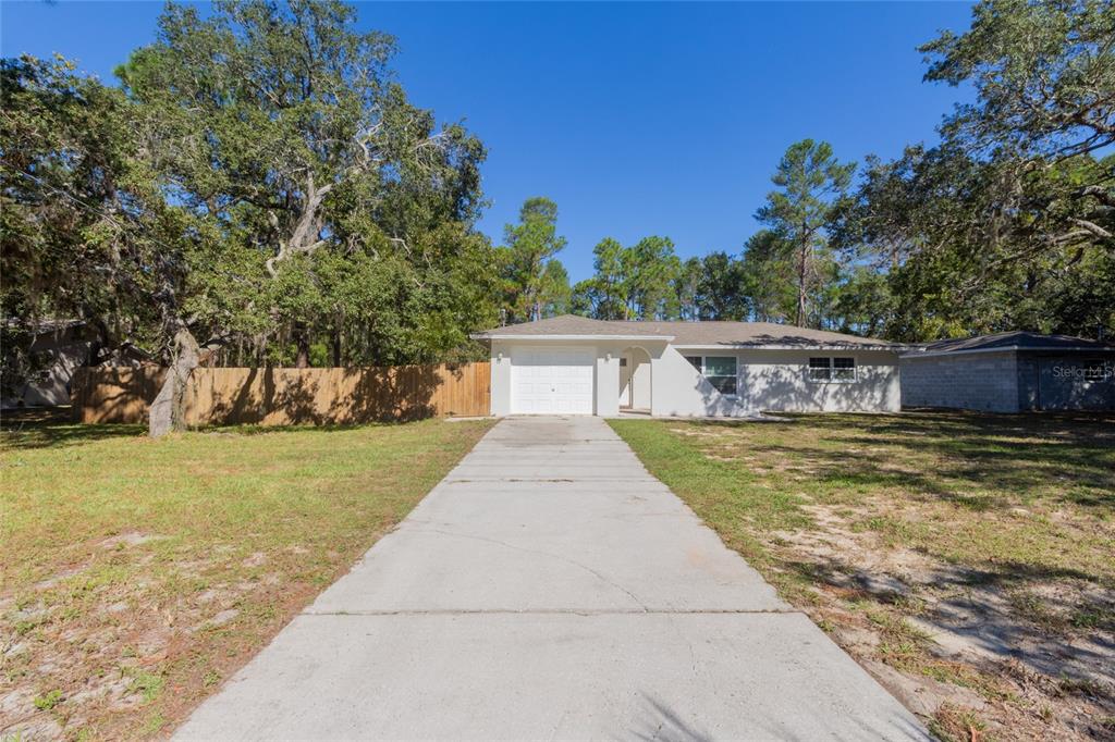 A single-story house with a white exterior, a concrete driveway, and a wooden fence — 6447 BRANDY DRIVE, SPRING HILL, FL