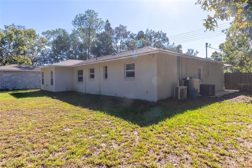 The exterior rear view of a single-story house with a lawn and trees — 6447 BRANDY DRIVE, SPRING HILL, FL