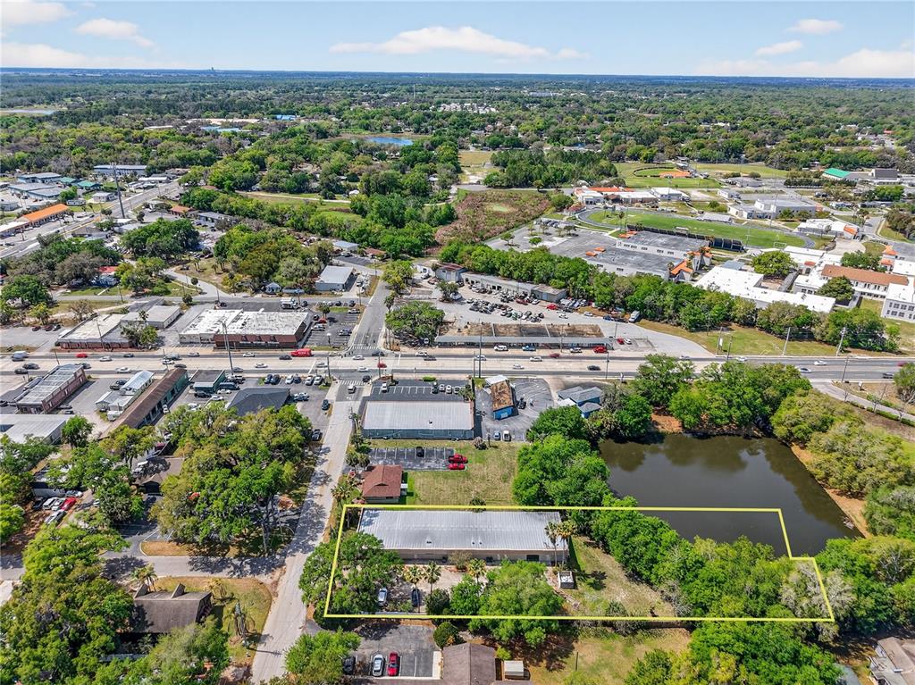 An aerial view shows a commercial building with a parking lot next to a pond — 1314 SUMTER STREET, LEESBURG, FL