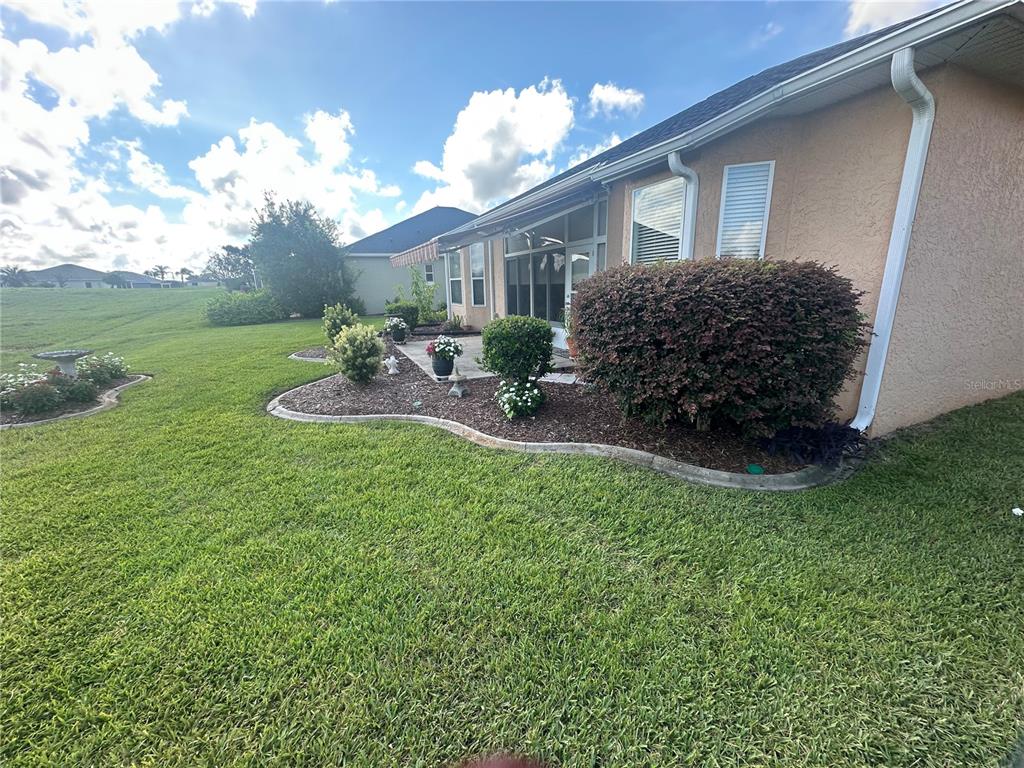 A view of a house exterior with a landscaped garden bed and a grassy lawn — 12173 SE 178TH STREET, SUMMERFIELD, FL