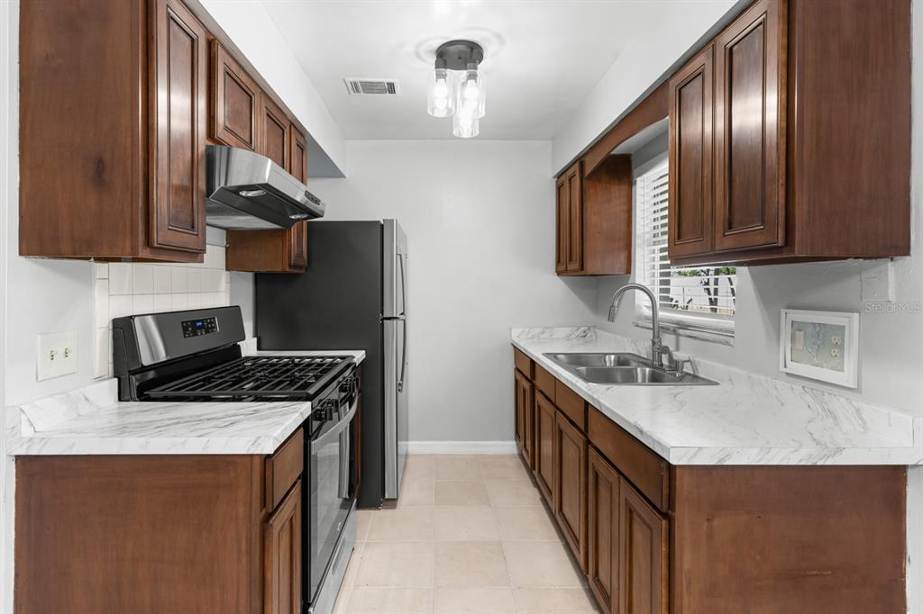 A galley kitchen features dark wood cabinets, white marble-look countertops, and stainless steel appliances — 610 E HELM WAY, CASSELBERRY, FL