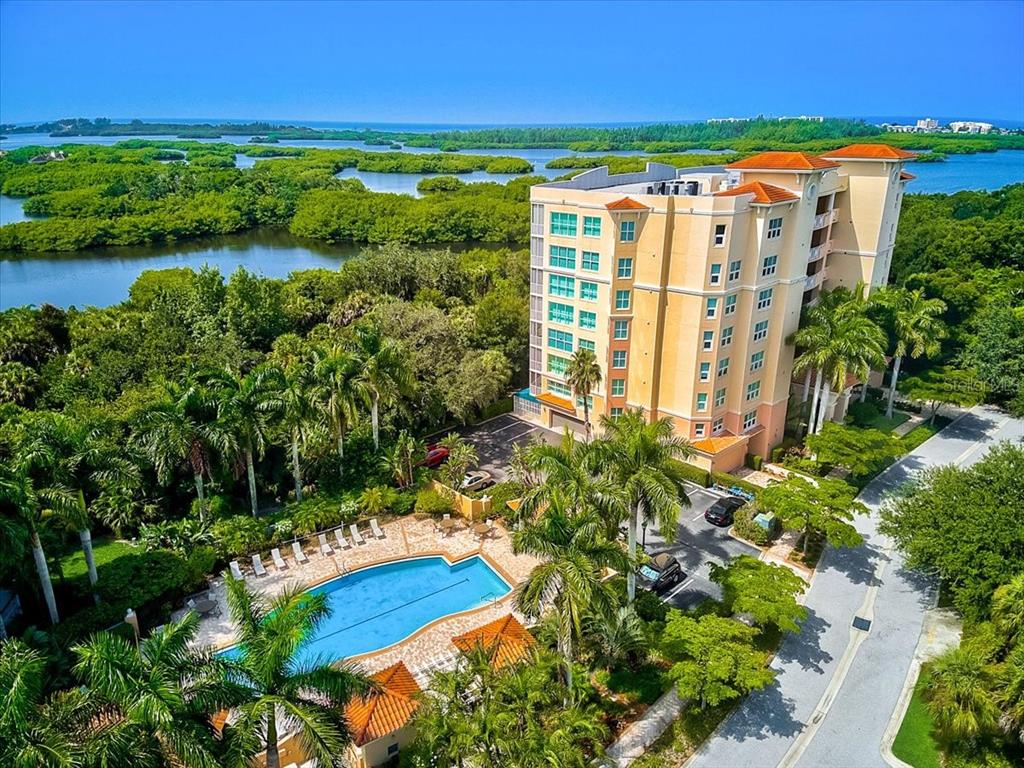 An aerial view of a multi-story apartment building with a swimming pool and surrounding greenery — 3603 N POINT ROAD UNIT 702, OSPREY, FL