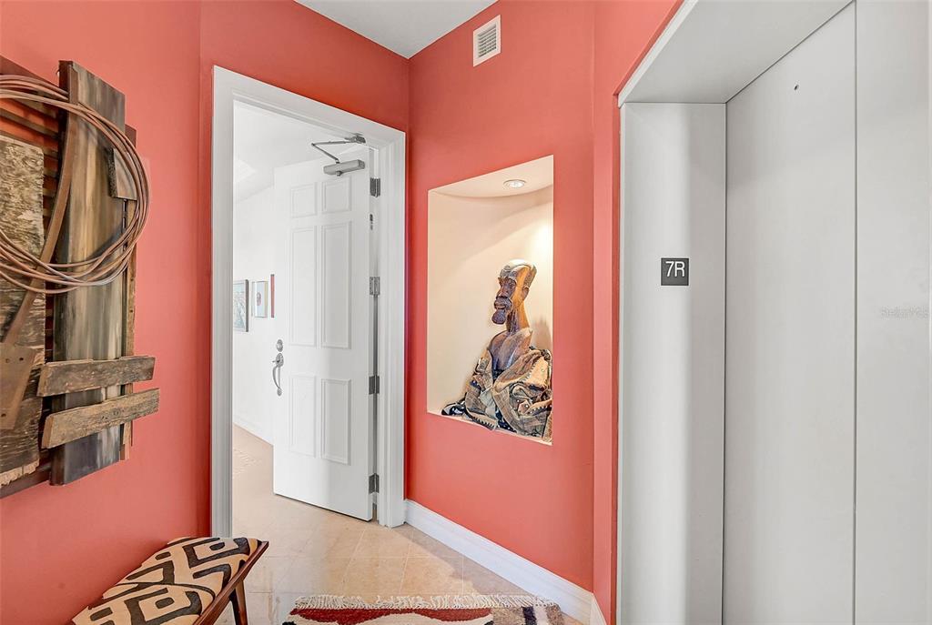 A hallway with coral walls features an elevator, a recessed wall niche, and a doorway — 3603 N POINT ROAD UNIT 702, OSPREY, FL