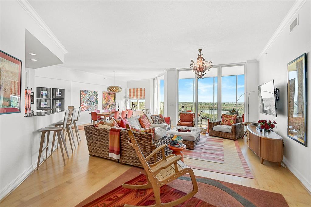 A bright, open-concept living and dining area features hardwood floors, wicker furniture, and floor-to-ceiling windows — 3603 N POINT ROAD UNIT 702, OSPREY, FL