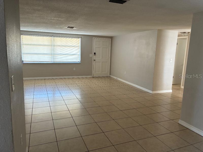 An empty room with light-colored tile flooring, beige walls, a window with blinds, and a door — 9425 LIDO LANE, PORT RICHEY, FL