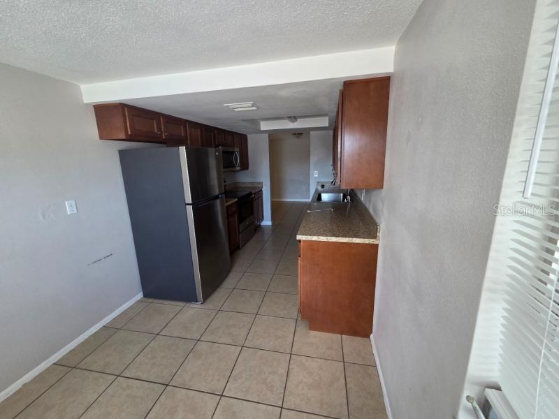 A kitchen features dark wood cabinets, stainless steel appliances, granite countertops, and tile flooring — 9425 LIDO LANE, PORT RICHEY, FL
