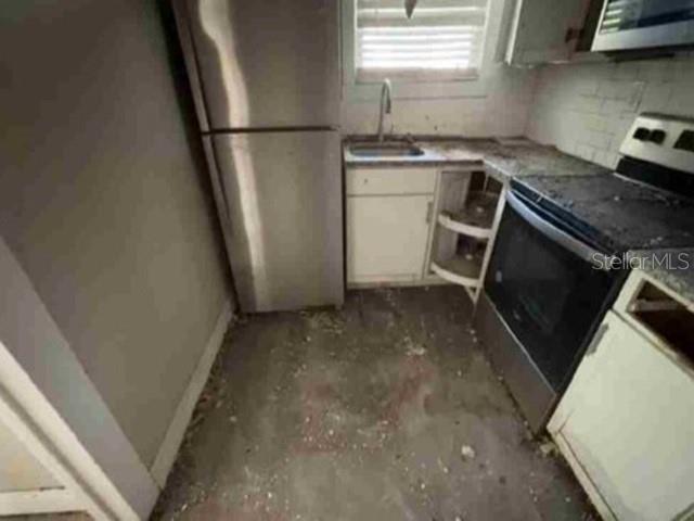 A small, unfinished kitchen features a stainless steel refrigerator, a sink, and a black stove — 2623 E 29TH AVENUE, TAMPA, FL