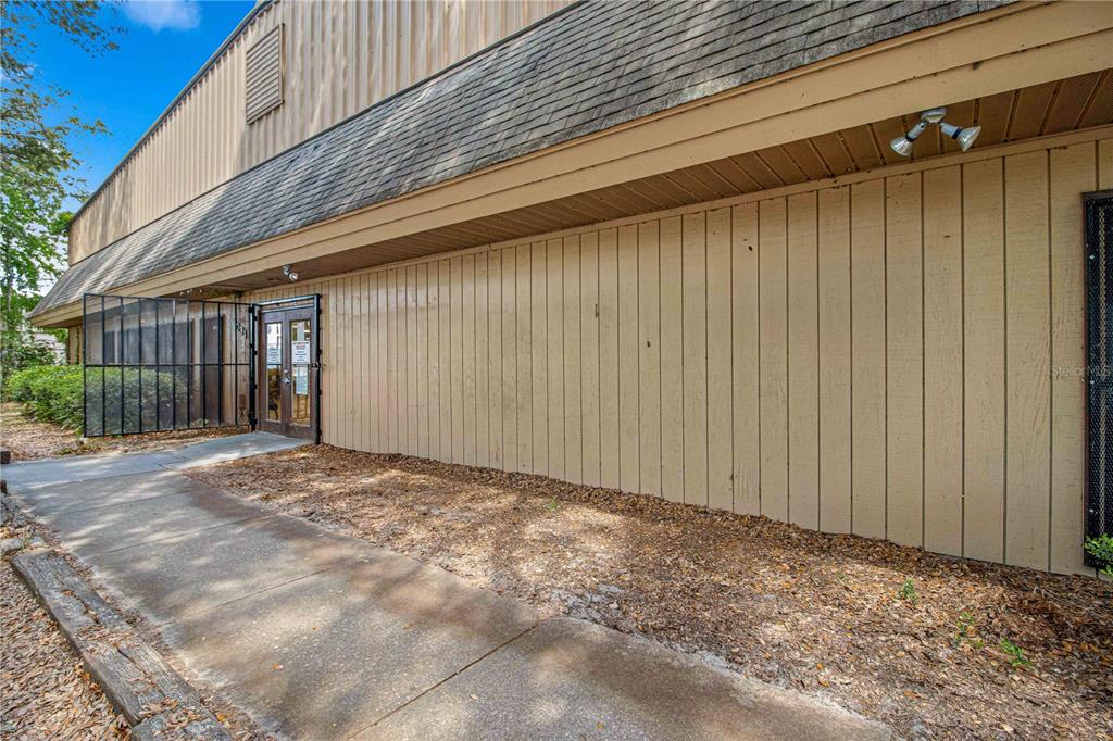 A tan vertical-sided building exterior features a concrete walkway, a dark door, and shingles — 1031 NE 16TH STREET, OCALA, FL