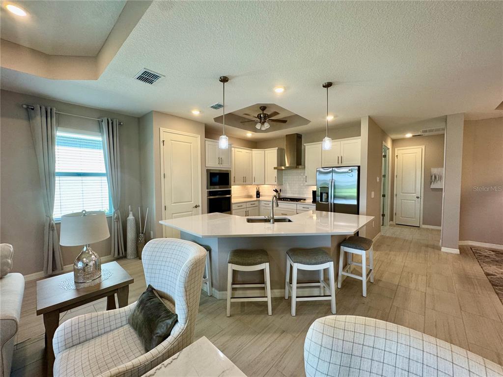 A kitchen features white cabinets, a quartz island with bar seating, and stainless steel appliances — 19140 CHERRYSTONE WAY, LAKEWOOD RANCH, FL