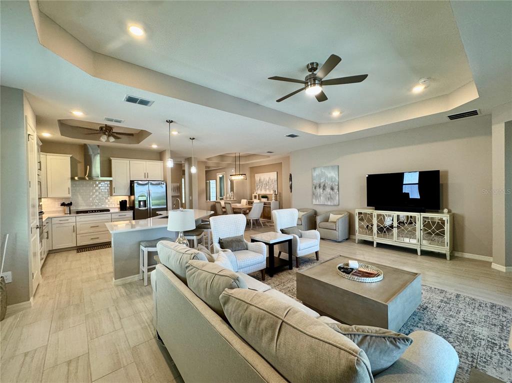 An open-concept living room and kitchen featuring light tile floors and a tray ceiling — 19140 CHERRYSTONE WAY, LAKEWOOD RANCH, FL