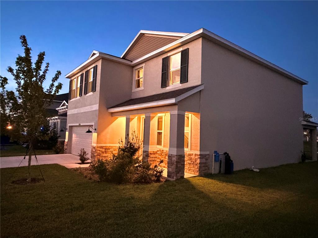 A two-story house exterior features a garage, stone accents, and a covered front porch at dusk — 11304 SPOONBILL FLOCK WAY, SAN ANTONIO, FL