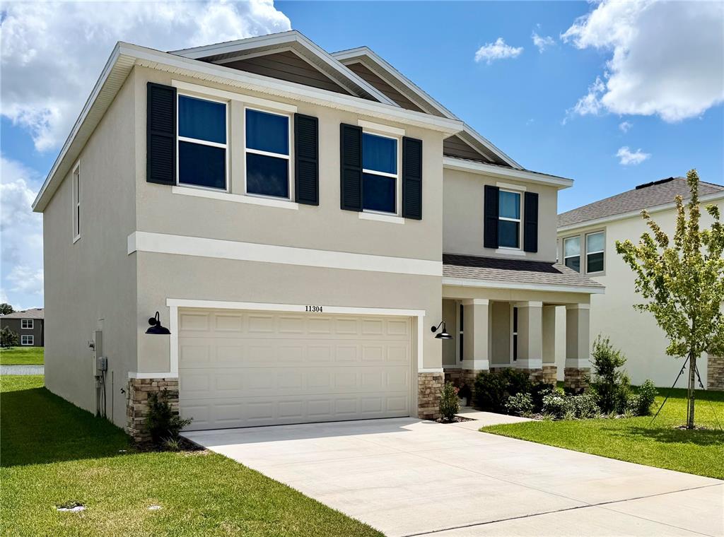 A two-story suburban house features a beige stucco exterior, a two-car garage, and dark shutters — 11304 SPOONBILL FLOCK WAY, SAN ANTONIO, FL