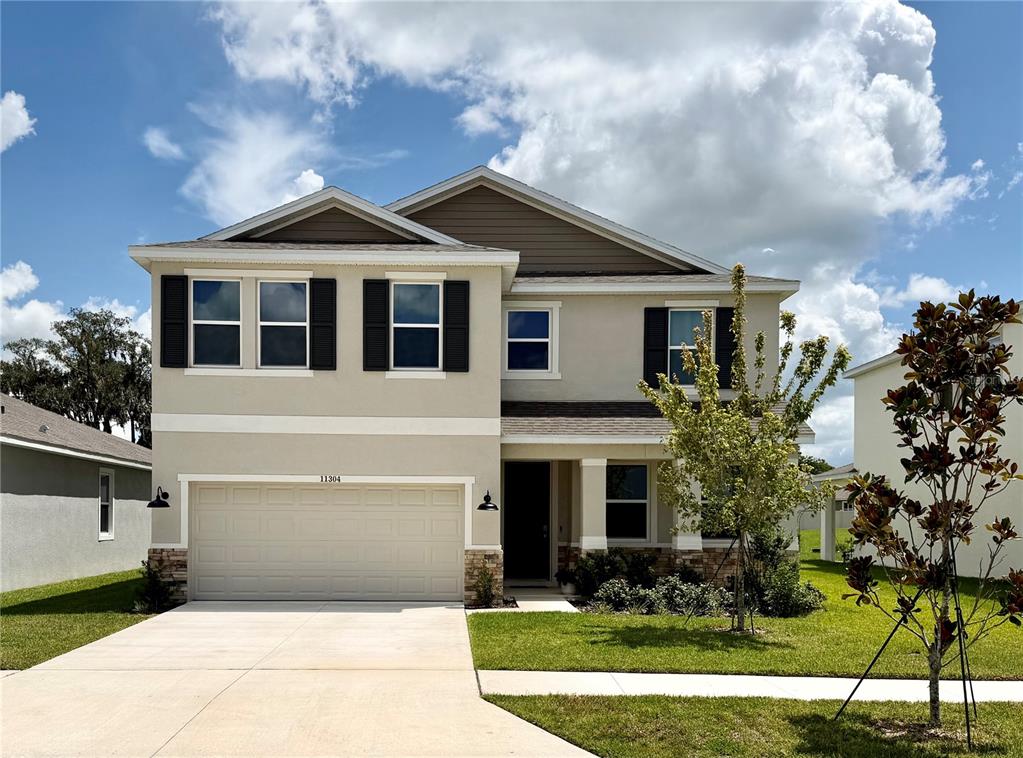 A two-story suburban house features a beige stucco exterior, a two-car garage, and dark shutters — 11304 SPOONBILL FLOCK WAY, SAN ANTONIO, FL