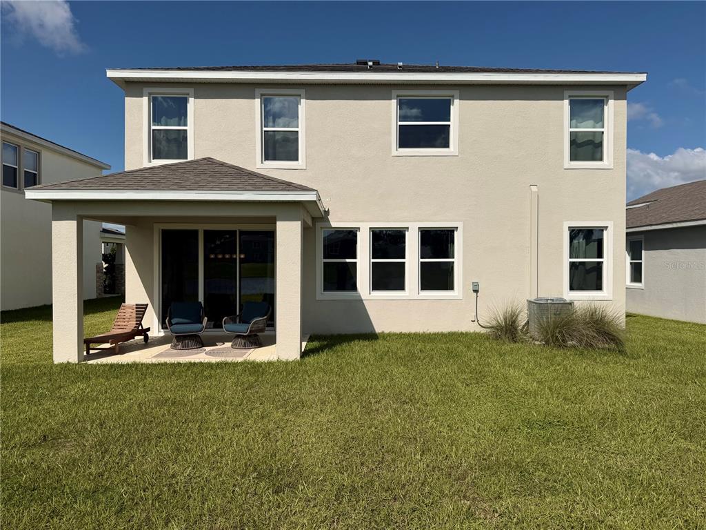 The rear exterior of a two-story house features a covered patio and a grassy yard — 11304 SPOONBILL FLOCK WAY, SAN ANTONIO, FL