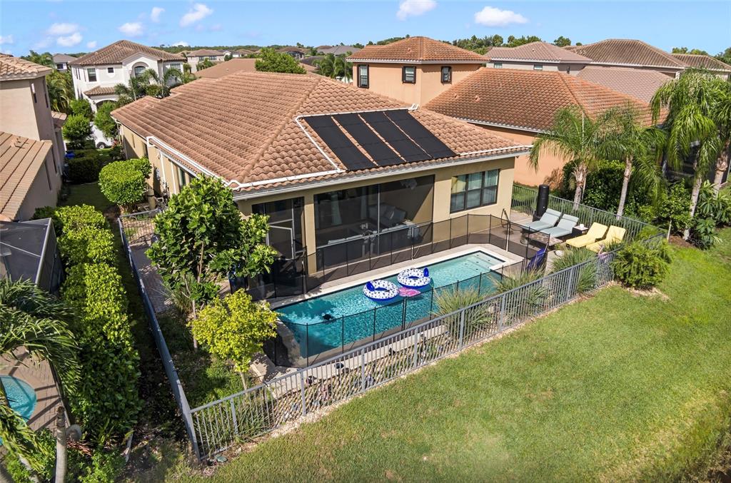 An aerial view of a house with a screened pool, solar panels, and fenced yard — 10035 CHESAPEAKE BAY DRIVE, FORT MYERS, FL