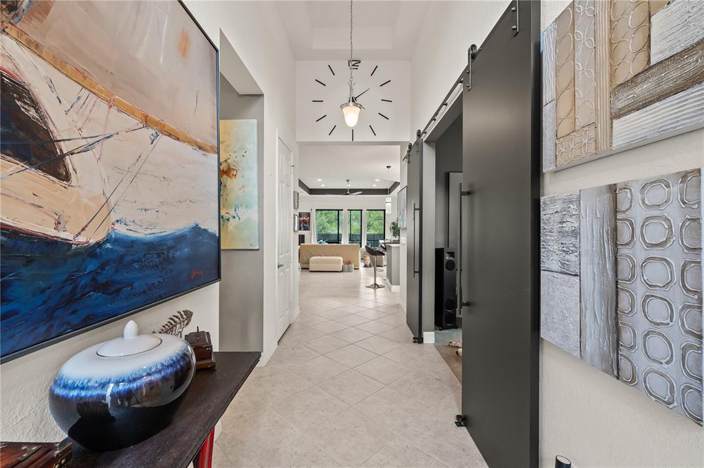 A hallway with tile floors leads toward an open living area featuring a large wall clock — 10035 CHESAPEAKE BAY DRIVE, FORT MYERS, FL