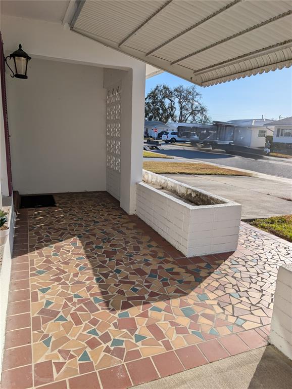 A covered porch features a multi-colored mosaic tile floor and a white brick planter box — 10139 44TH WAY N, PINELLAS PARK, FL