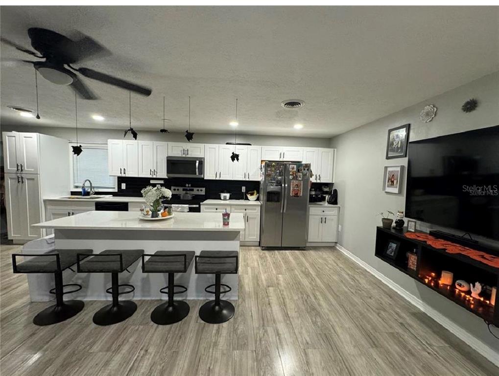 A modern kitchen features white cabinetry, a central island with bar stools, and wood flooring — 5832 HOLMES DRIVE, ORLANDO, FL