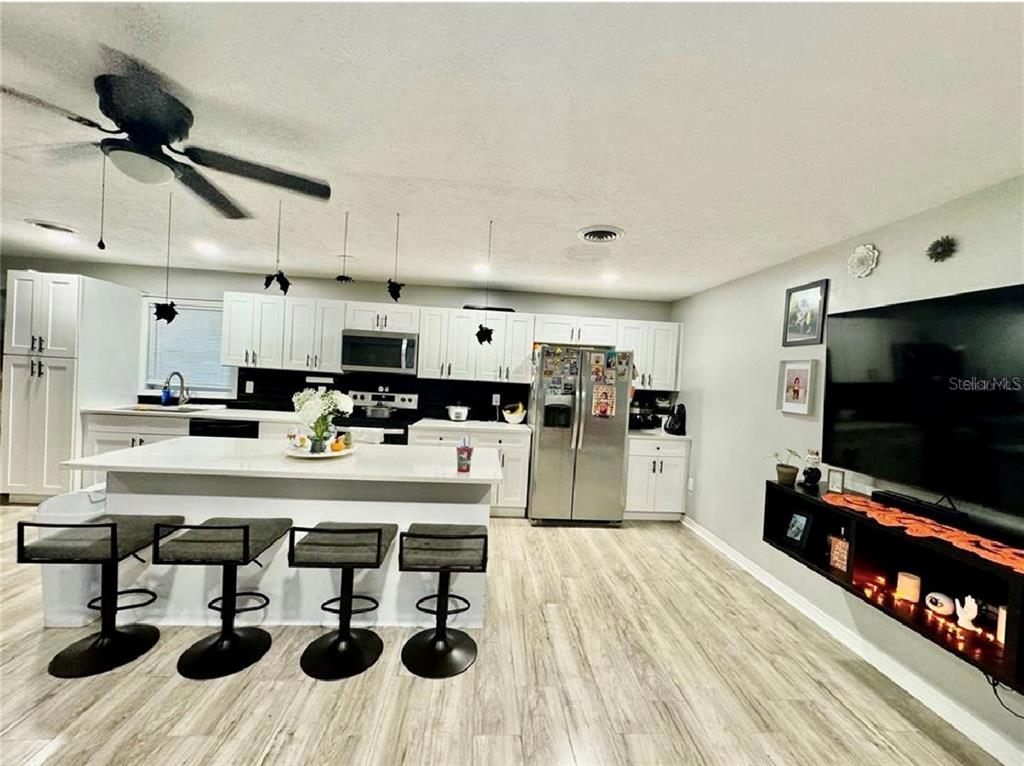A kitchen with white cabinets, a central island with bar seating, and a living area — 5832 HOLMES DRIVE, ORLANDO, FL